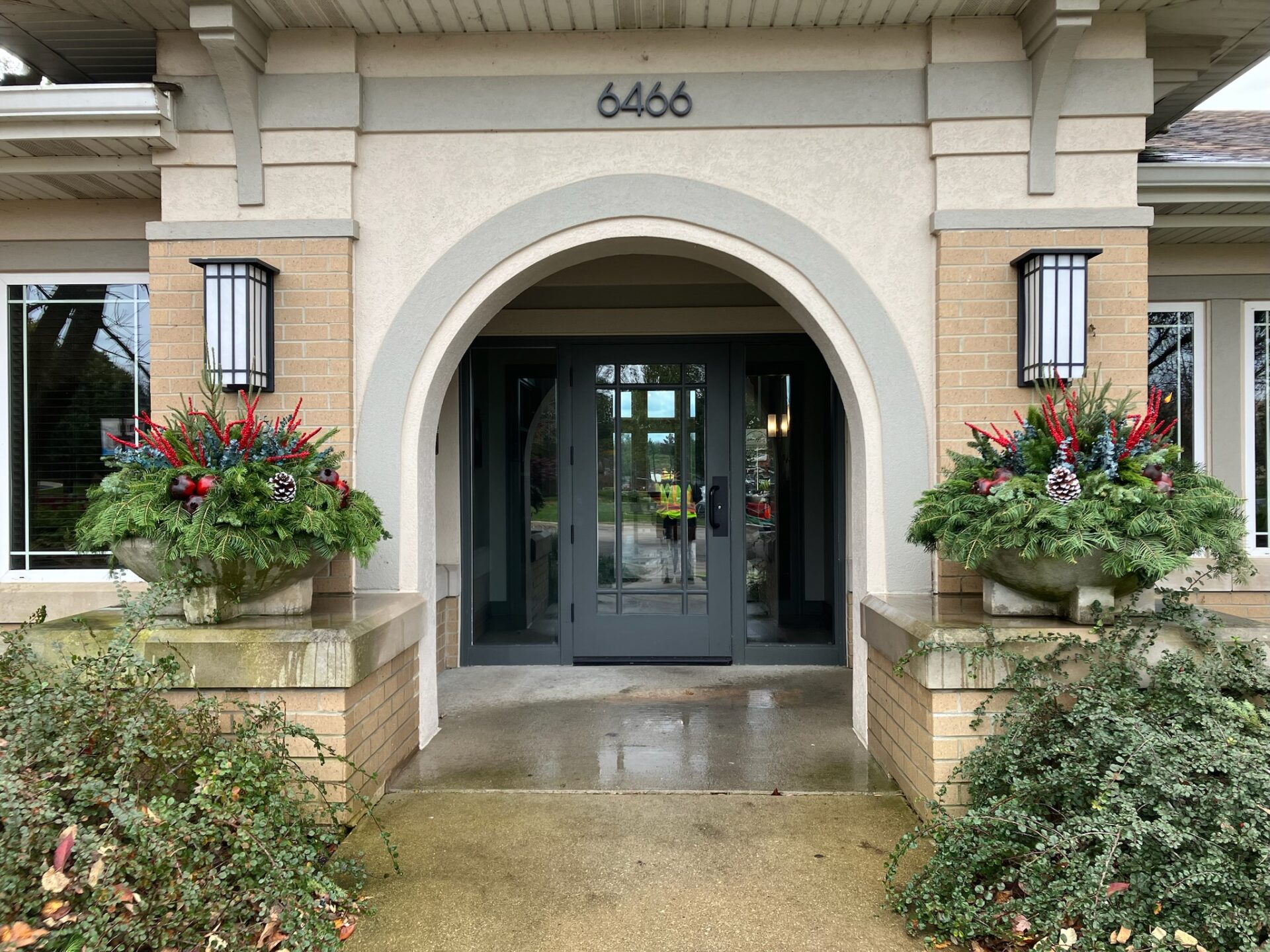 Entrance with arched doorway and number 6466. Two large planters hold festive greenery and pine cones, flanking the doorway.