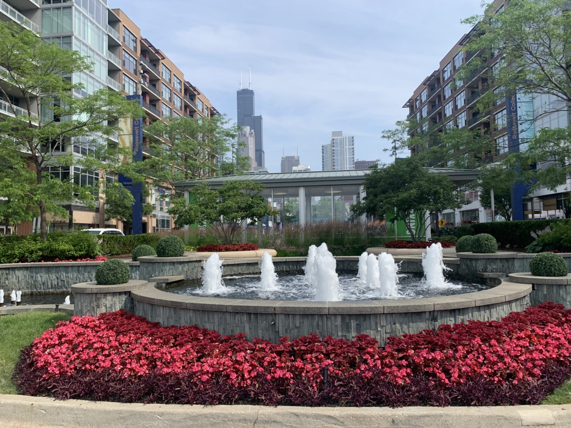 A fountain surrounded by vibrant flowers and trees is in a landscaped plaza with the Willis Tower visible in the background.