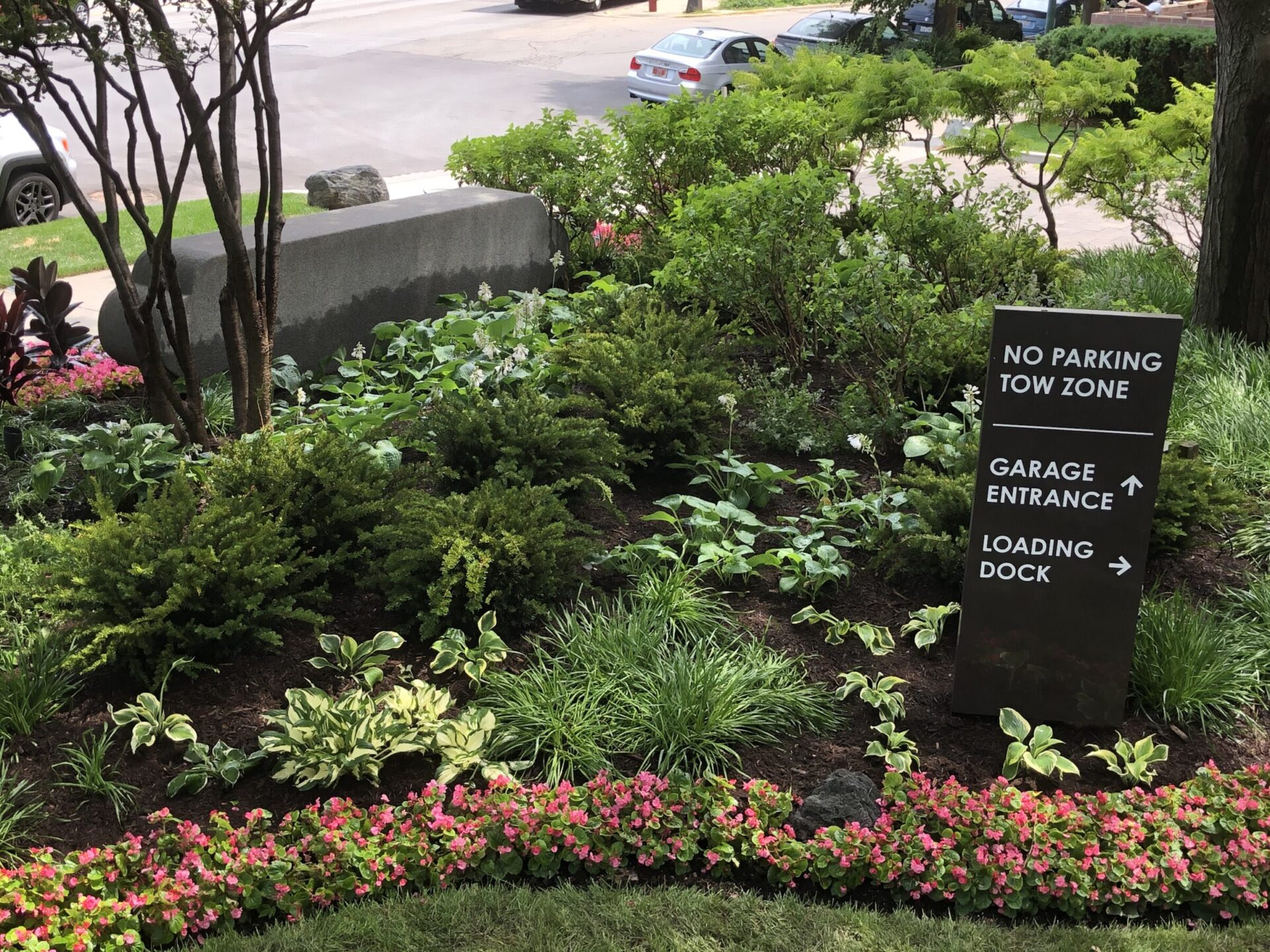 Lush garden with a sign directing to a garage entrance and loading dock. Curved bench and cars are visible in the background.