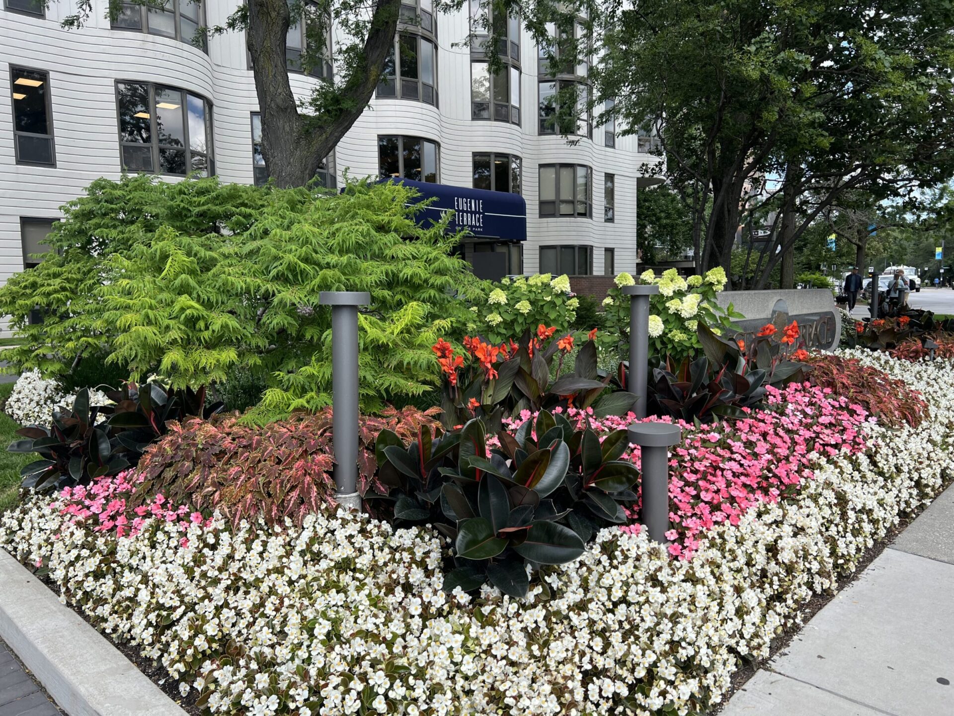 A vibrant flower bed with colorful blooms is in front of a modern building named Eugene Field Terrace, surrounded by trees and greenery.