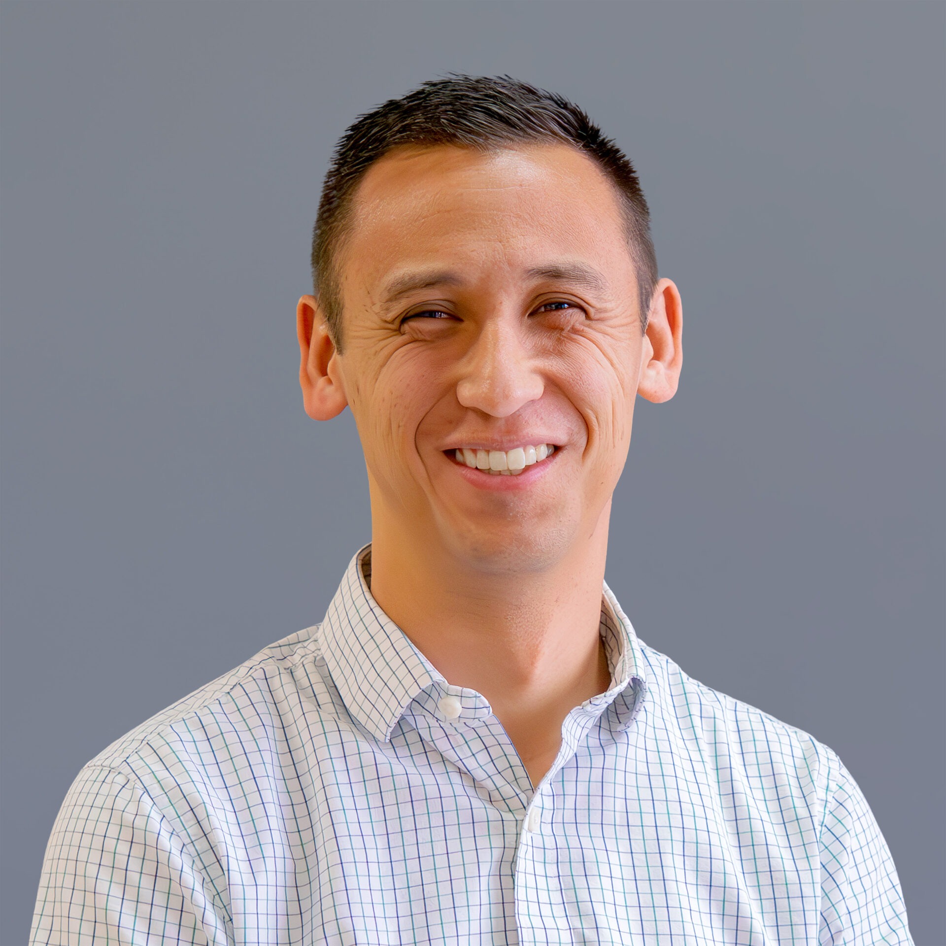 A smiling person wearing a checked shirt is in front of a plain grey background. There are no recognizable landmarks or historical buildings.