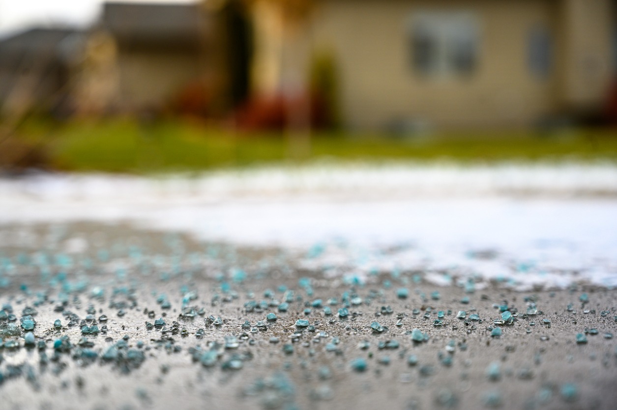 A close-up of blue rock salt scattered on a concrete surface, with a blurred background of grass and a house.